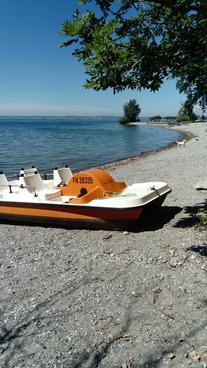 A boat with the registration number FN 28335 on a pebbled shore by a calm body of water.