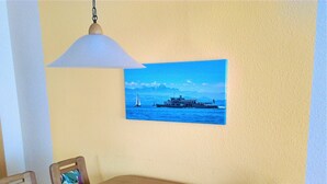 En matplats med ett träbord och stolar, en hängande lampa och en målning som föreställer en båt på vattnet.