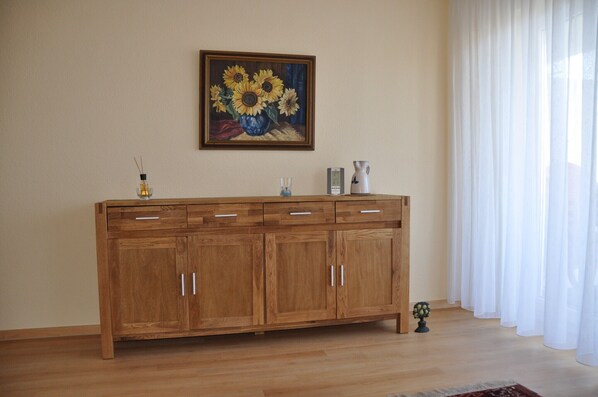A wooden cabinet with drawers, a framed painting of sunflowers, and a white curtain.