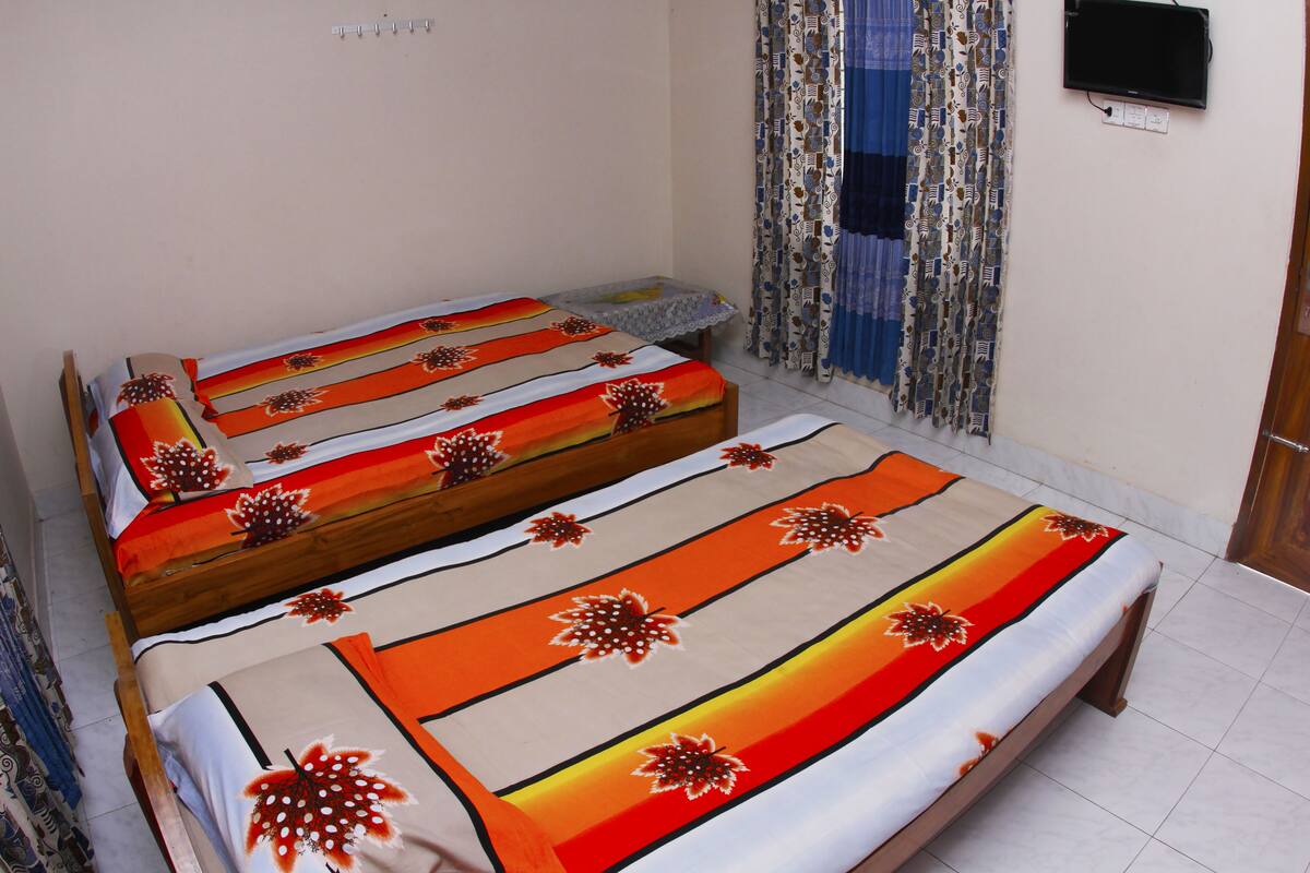 A room with two single beds, a small table, and a wall-mounted TV.