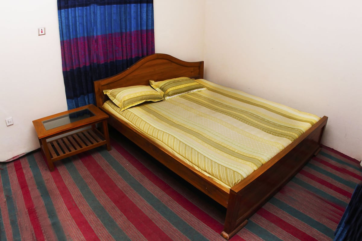 A single bed with a wooden frame, a bedside table with a glass top, and a striped carpet.