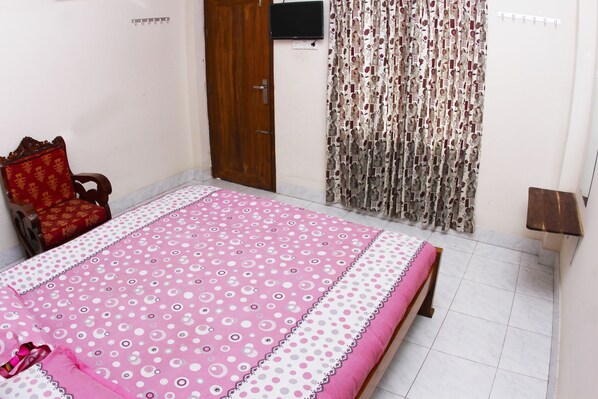 Un dormitorio con cama, una puerta de madera, televisor montado en la pared y cortina estampada.