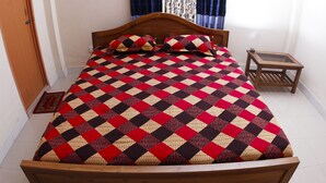 A neatly made bed with a checkered bedspread, a wooden headboard, and a small wooden nightstand beside it.