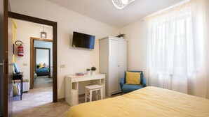 Un dormitorio con cama, escritorio, armario, televisor y ventana con cortinas.