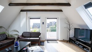 Una sala de estar moderna con techo inclinado, televisor de pantalla plana, sofás de cuero, una mesa de centro y un ventanal con vistas a edificios.