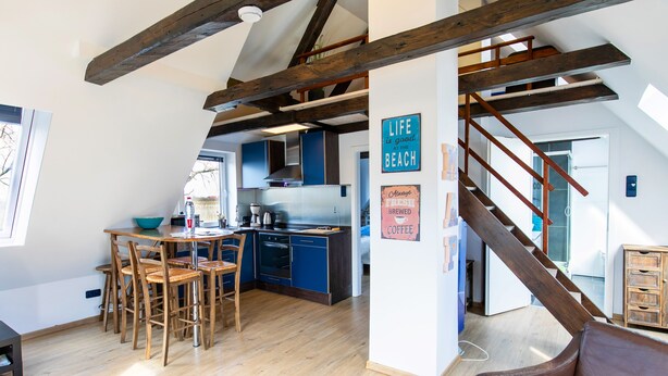 Una cocina amplia con vigas de madera, un comedor con sillas y una escalera que conduce a otro nivel.