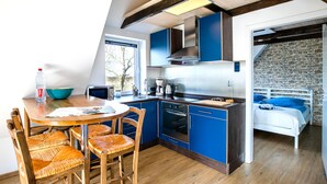 Una cocina moderna con armarios azules, una mesa de comedor de madera con sillas y vistas a una pared de piedra a través de un vano abierto.