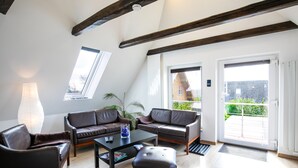Una sala de estar moderna con techo alto, vigas de madera, dos sofás de cuero, una mesa de centro y un amplio ventanal con vistas al exterior.