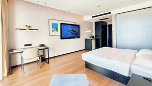 Een moderne hotelkamer met een bed, een bureau met stoel, een televisie en een kleine kitchenette.