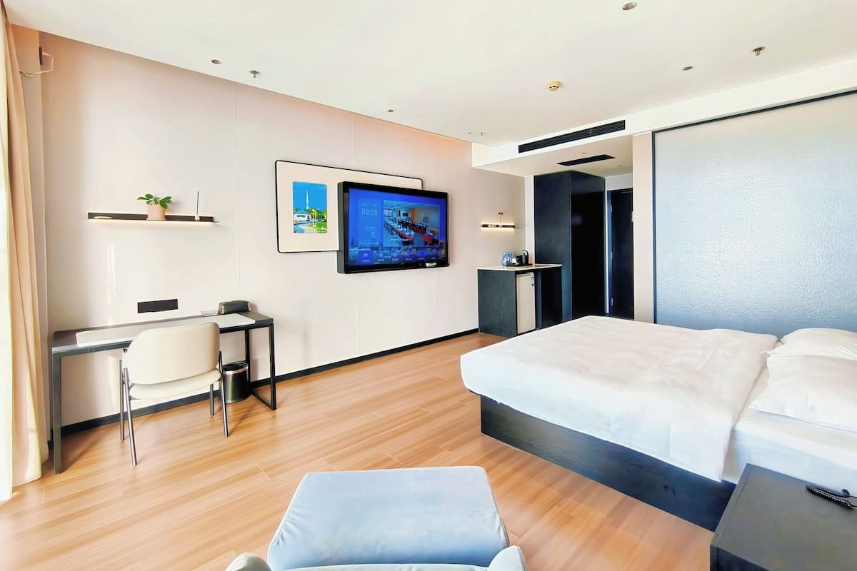 Een moderne hotelkamer met een bed, een bureau met stoel, een televisie en een kleine kitchenette.