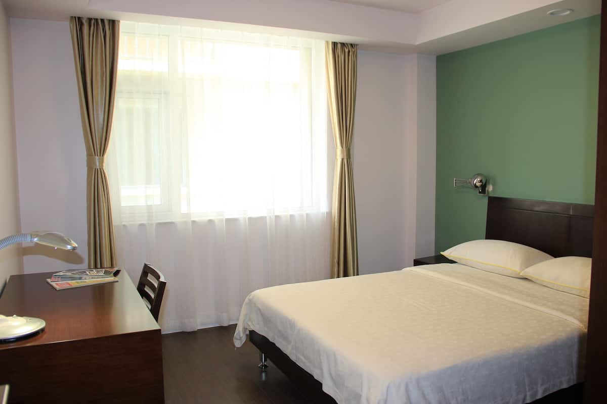 Een hotelkamer met een bed, een bureau met lamp, een stoel en een raam met gordijnen.