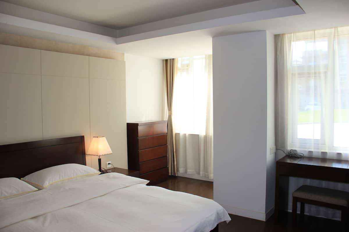 Een hotelkamer met een bed, een bureau, een kastje en een raam met gordijnen.