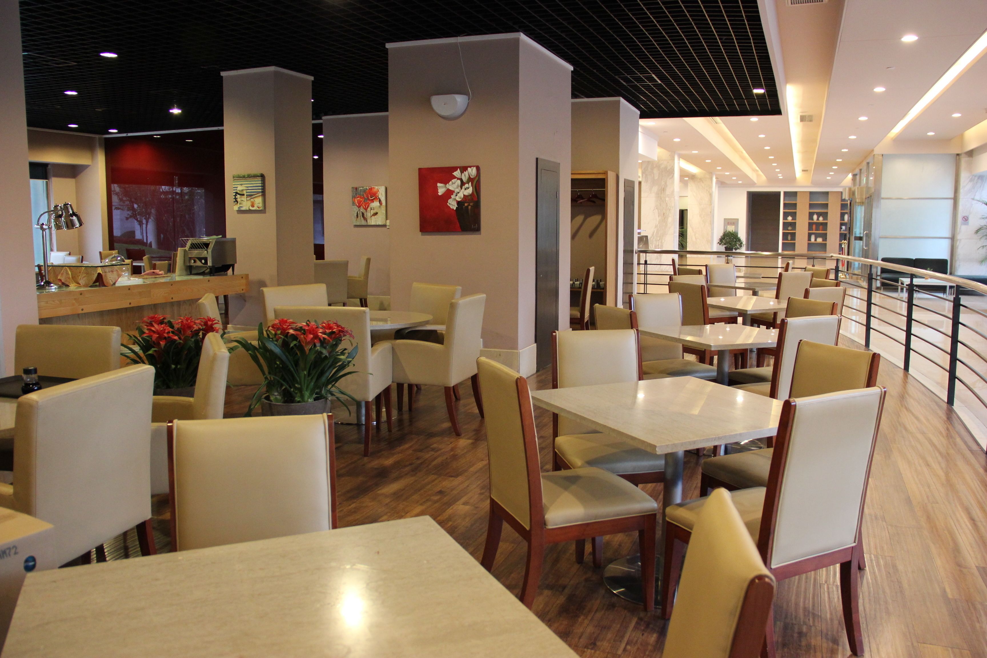 A modern dining area with multiple tables and chairs, a counter with a cash register, and a staircase leading to an upper level.