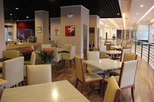 A modern dining area with multiple tables and chairs, a counter with a cash register, and a staircase leading to an upper level.