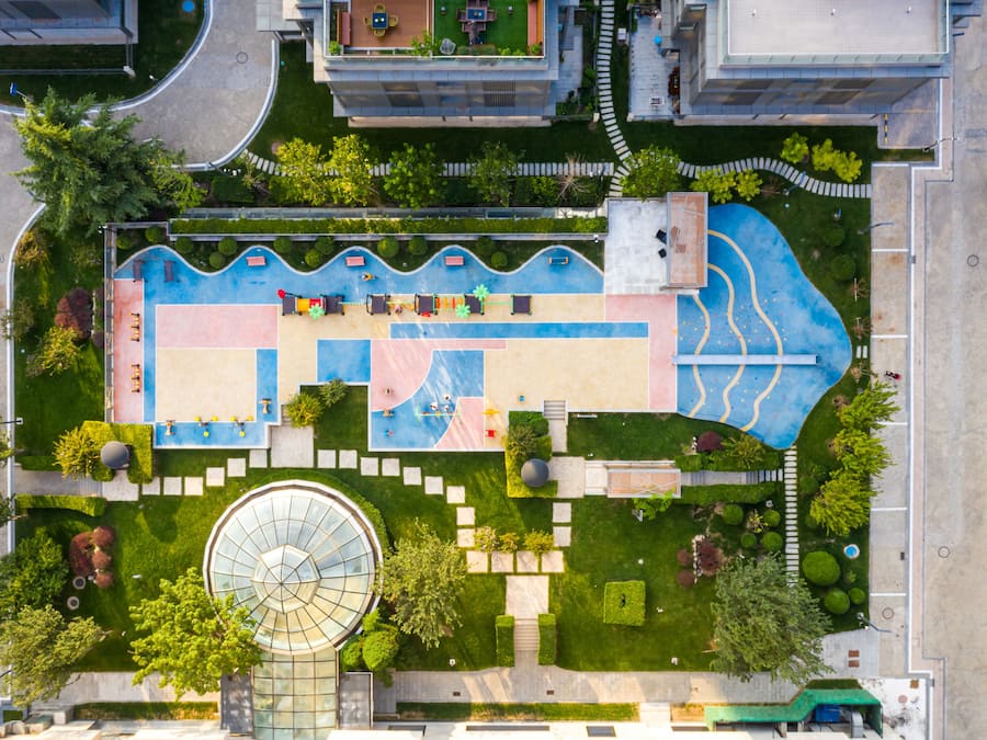 An aerial view of a modern building with a rooftop garden, a swimming pool, and a circular glass structure.