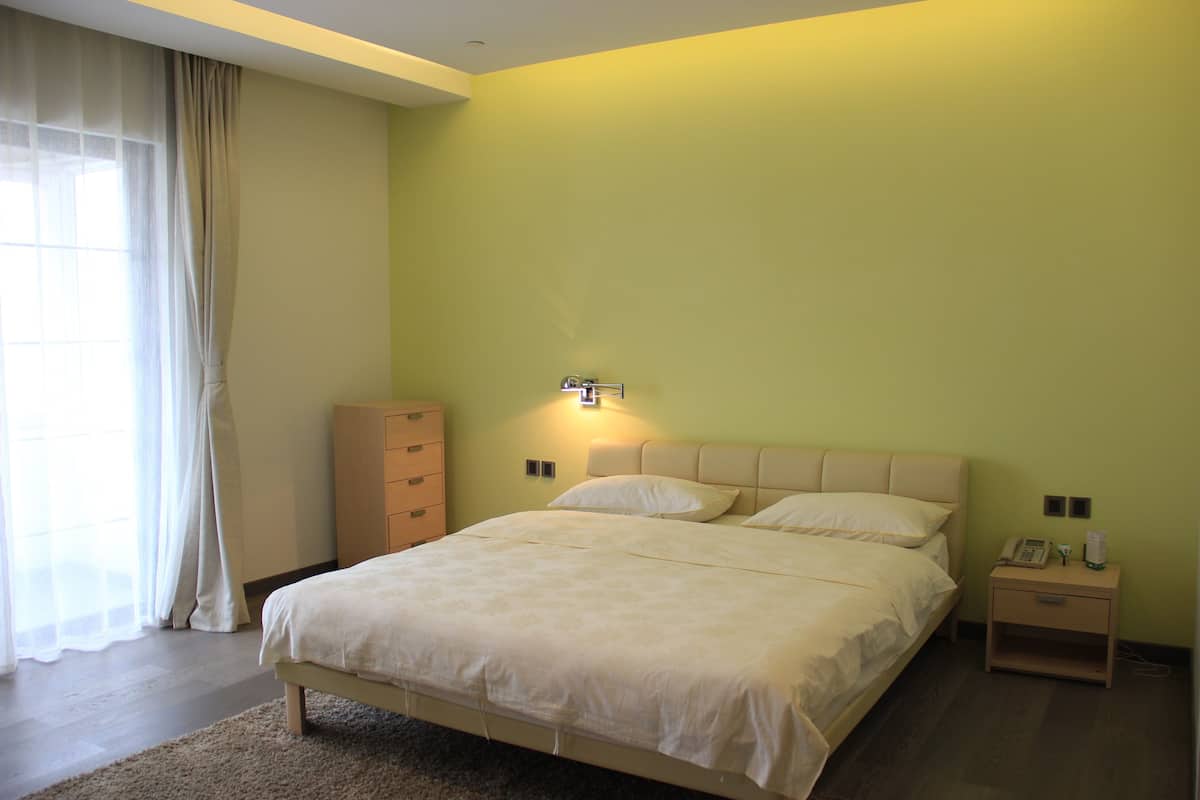 Een slaapkamer met een bed, nachtkastje, gordijnen en een raam.