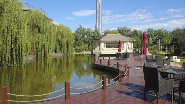 A riverside deck with a restaurant, outdoor seating, and a tall tower in the background. - GreenPark Hotel Tianjin (Tianjin)