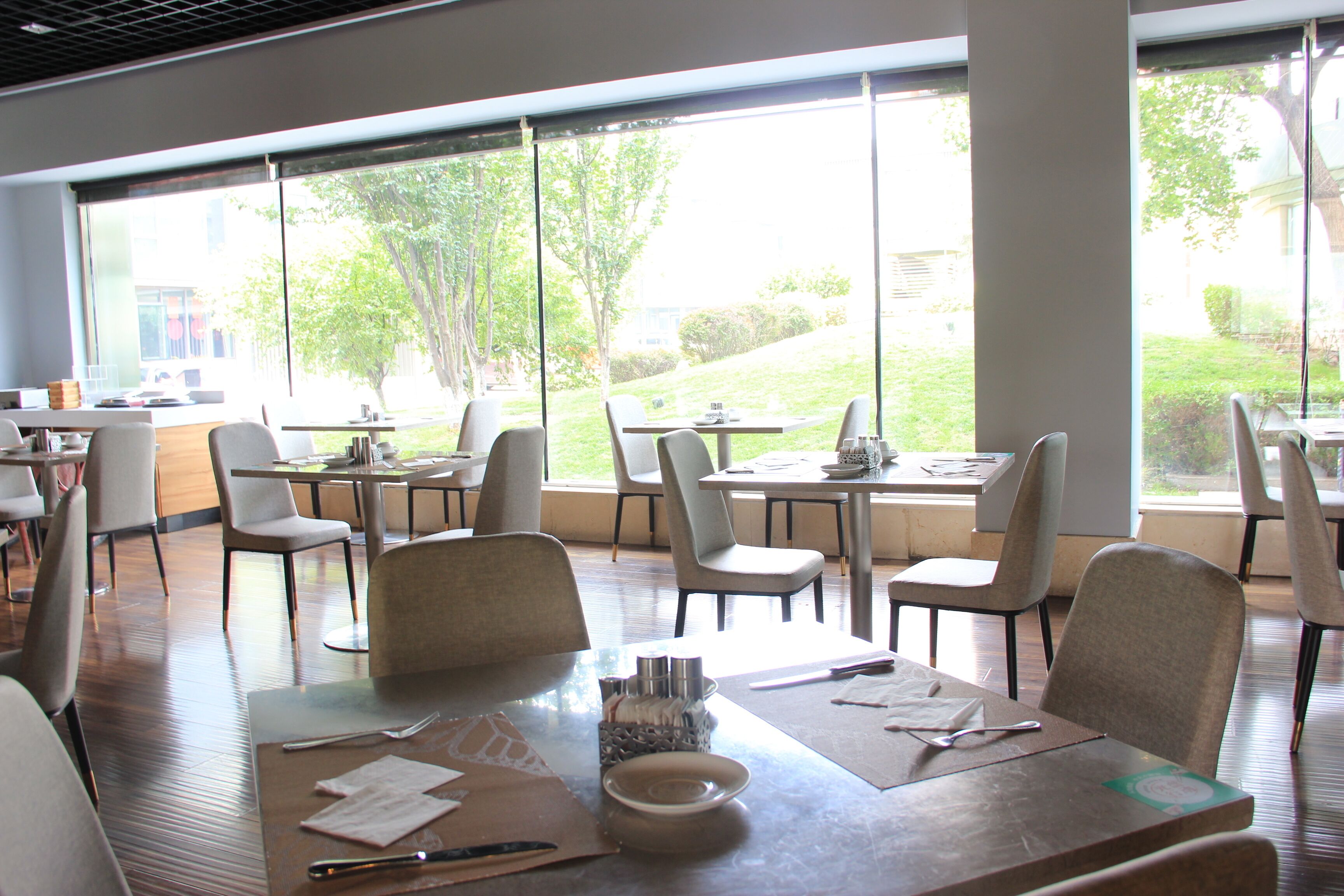 A modern dining area with large windows, wooden tables, and comfortable chairs.