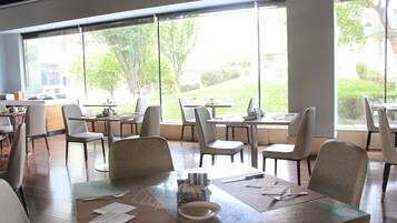 A modern dining area with large windows, wooden tables, and comfortable chairs.