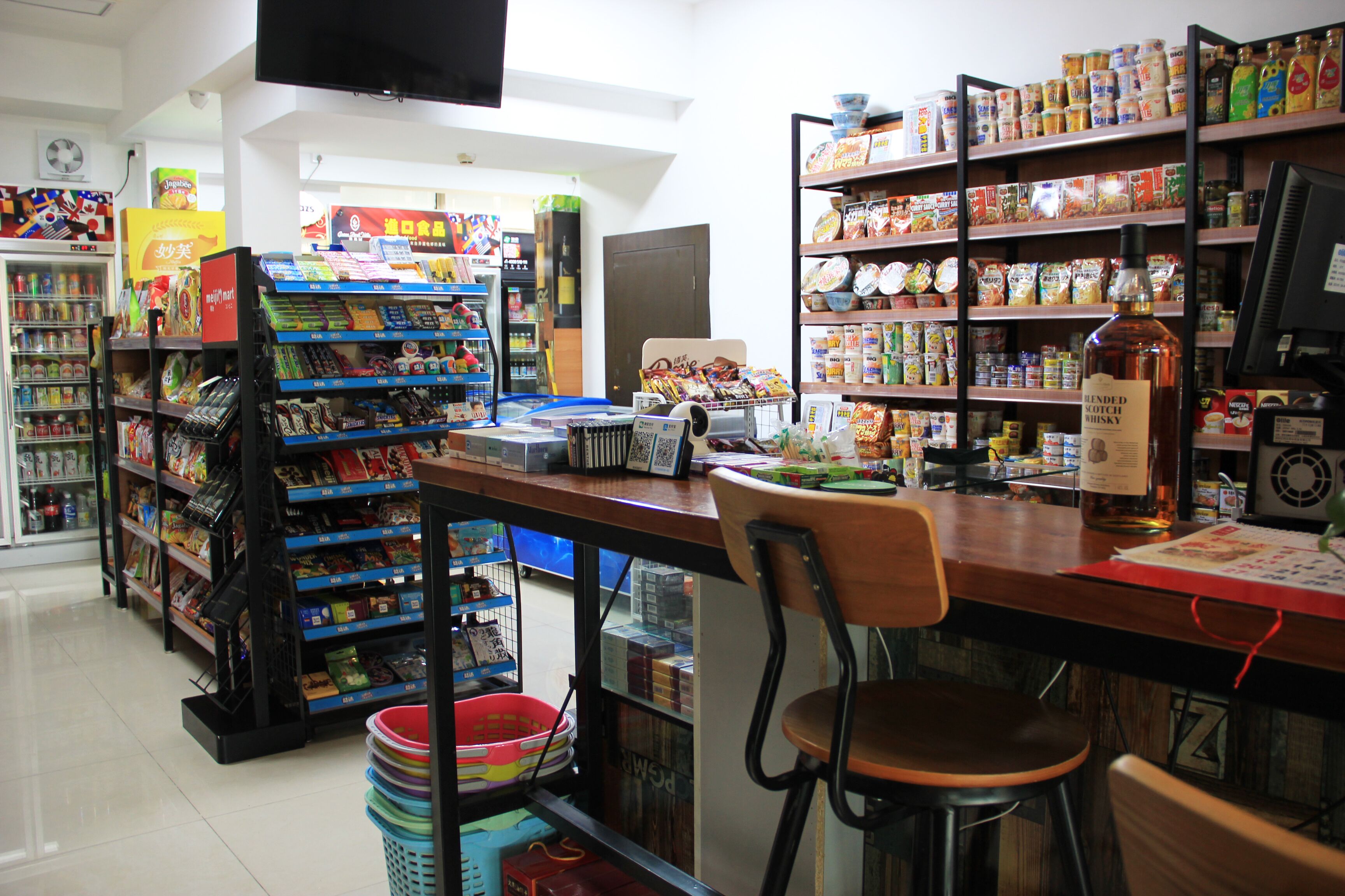 Una tienda de comestibles con estantes llenos de diversos productos, una caja registradora y una silla.
