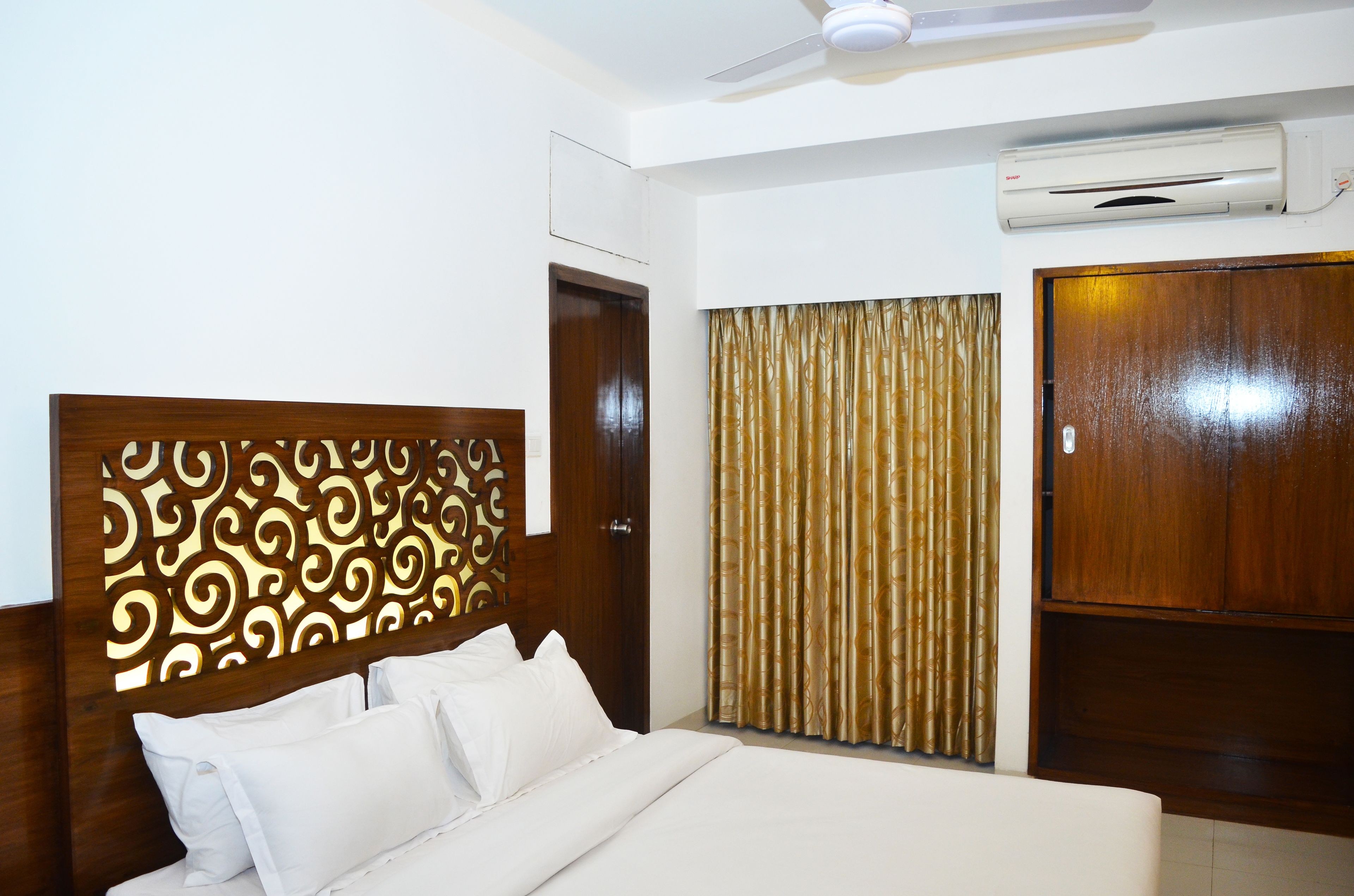 A hotel room with a bed, a ceiling fan, an air conditioning unit, and a wooden wardrobe.