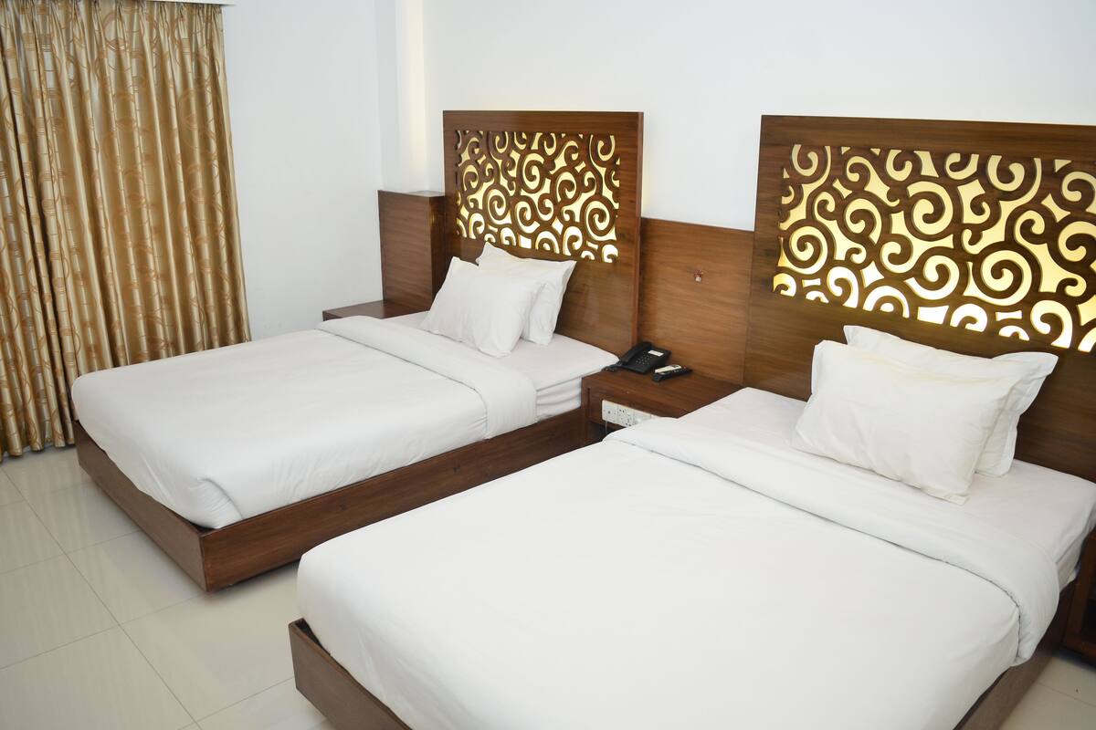 Habitación de hotel con dos camas individuales, cabeceros de madera y una cortina.