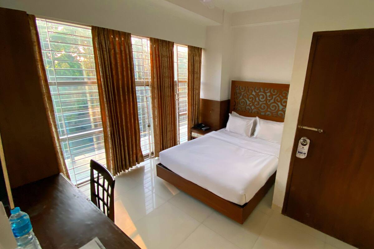 Una habitación de hotel con cama, escritorio, silla, mesita de noche y puerta.