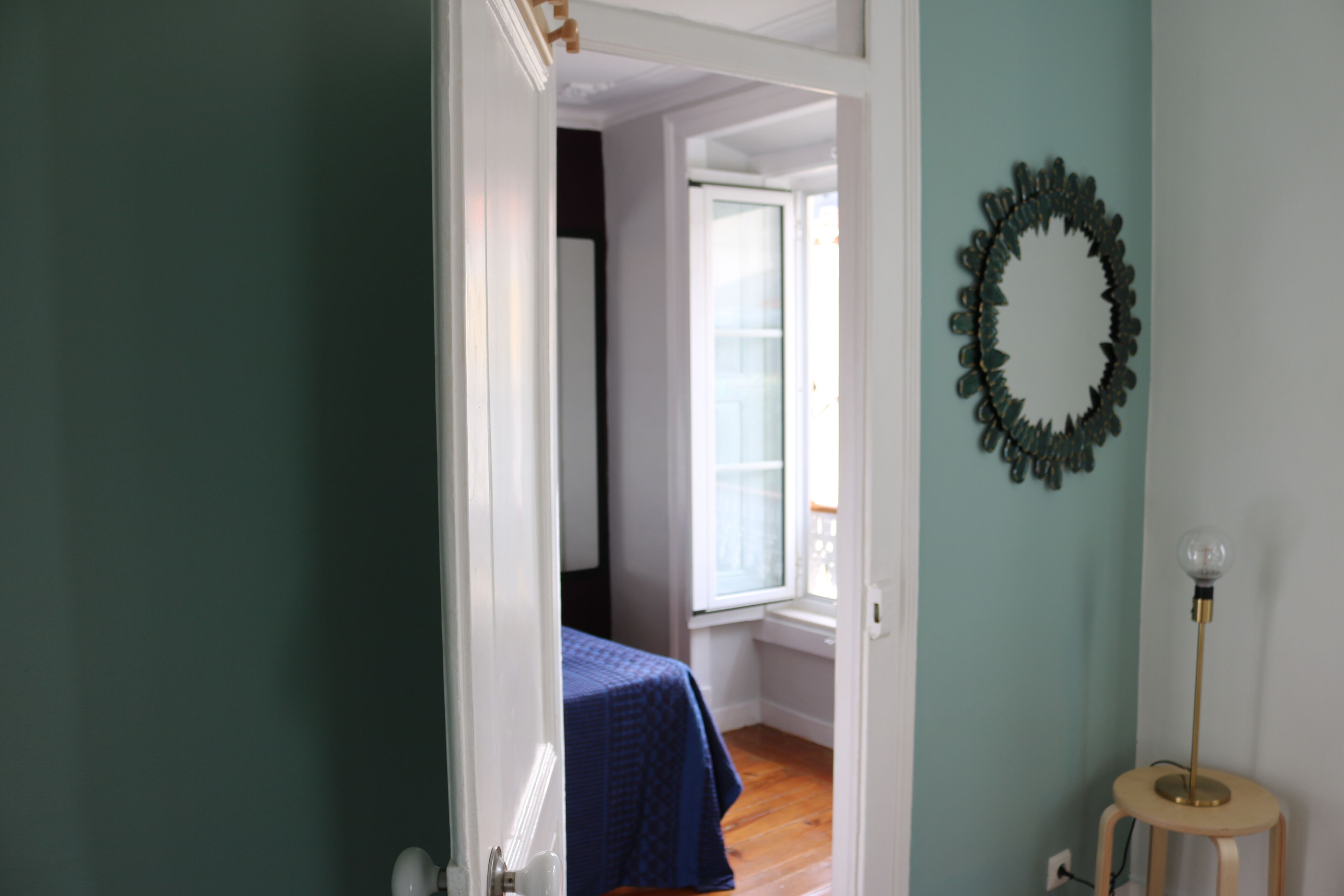 Une pièce comprenant un lit, une fenêtre, un miroir fixé au mur et une lampe sur pied.