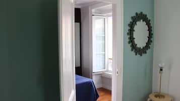 Une pièce comprenant un lit, une fenêtre, un miroir fixé au mur et une lampe sur pied.
