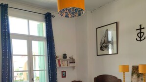 A bedroom with a bed, a wooden cabinet, a bookshelf, a window with curtains, and a hanging lamp. - Beautiful beachfront house with character (Le Grau-Du-Roi)