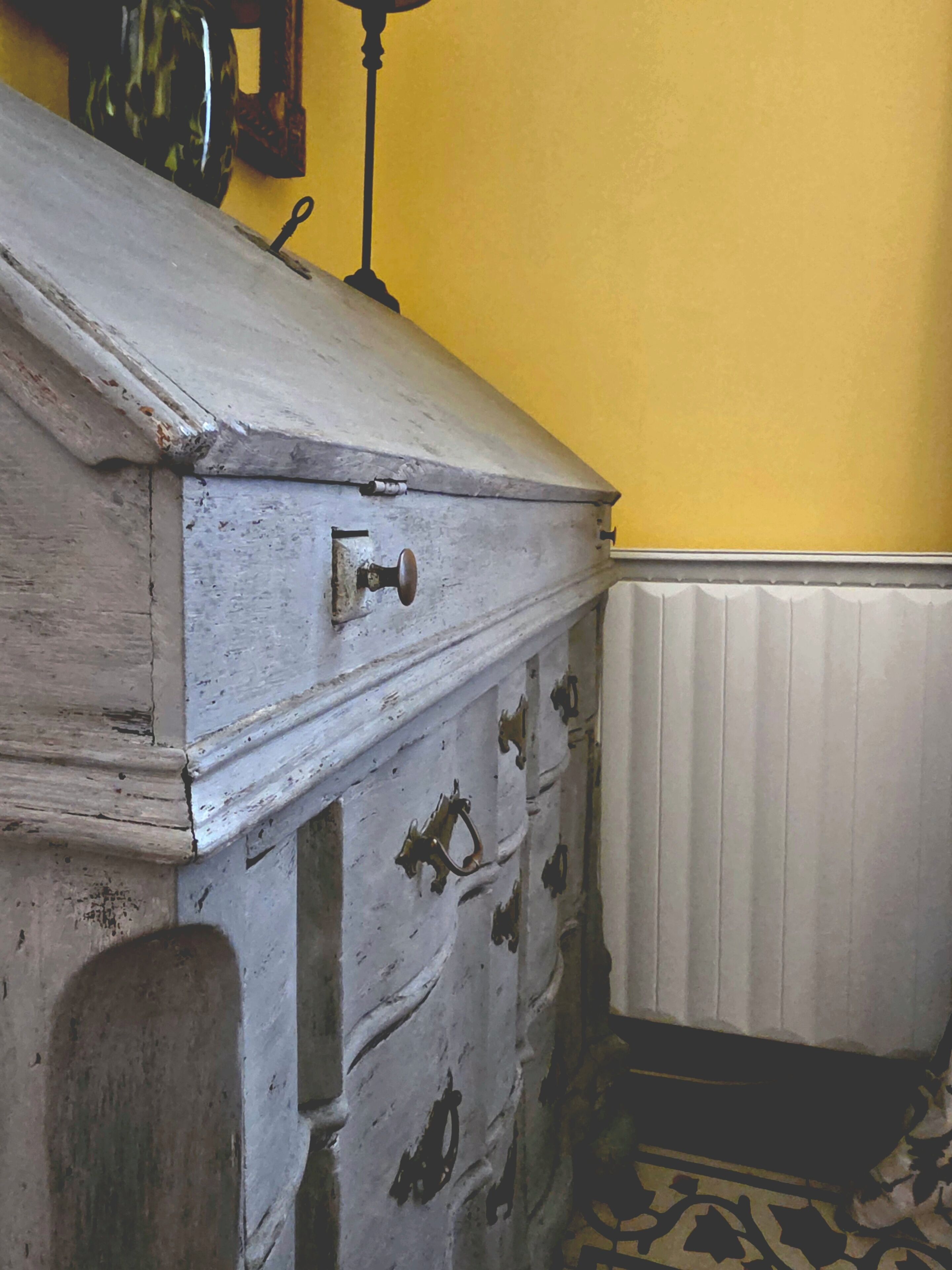 Une commode ancienne avec une poignée en laiton, un radiateur et un tapis à motifs.