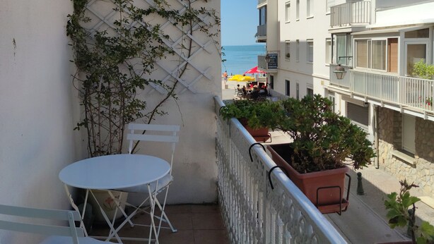 A balcony with a white table and chairs, potted plants, and a view of the sea and buildings. - Beautiful beachfront house with character (Le Grau-Du-Roi)