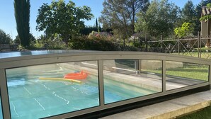 A swimming pool with a glass enclosure, surrounded by a stone wall and lush greenery. - Le Mas de Baptiste near the town center with heated, sheltered swimming pool (Saint-Rémy-De-Provence)