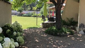 A patio area with a table and chairs, surrounded by greenery and a gravel path. - Le Mas de Baptiste near the town center with heated, sheltered swimming pool (Saint-Rémy-De-Provence)
