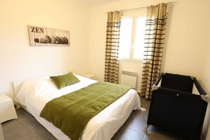A bedroom with a bed, a green throw blanket, a black chair, a radiator, and striped curtains.