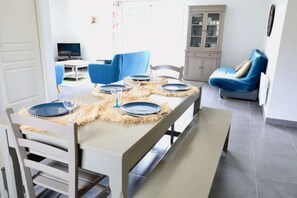 A dining area with a table set for four, a blue chair, a cabinet, and a television in the background.
