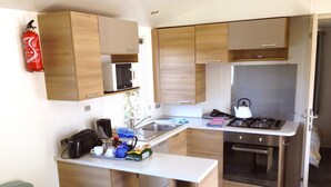 Una cocina compacta con armarios de madera, un microondas, una tetera y una estufa.
