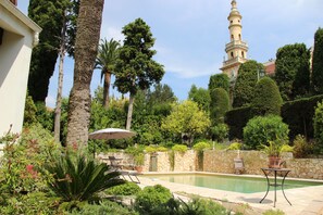 A pool area with a stone wall, palm trees, and a view of a tower. - "VILLA TSAVORITE - CANNES CALIFORNIE" : large swimming pool, 4 bedrooms & 210 m2. (Cannes)