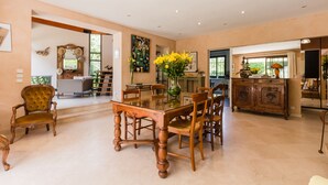 Un comedor amplio con una mesa de vidrio rodeada de sillas de madera, un aparador de madera y un jarrón con flores amarillas.