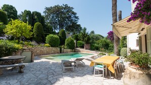 Una piscina con baldosas de piedra, rodeada por un patio con muebles de exterior y una pared de piedra.