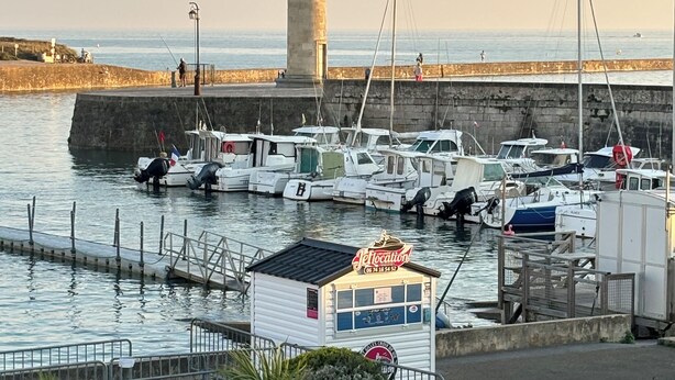 Ein Hafen mit vertäuten Booten, einem Leuchtturm und einem kleinen Gebäude mit der Aufschrift 'Jetlocation'.