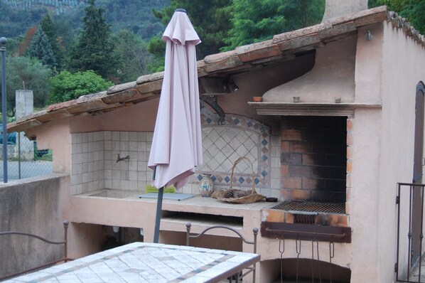 A rustic outdoor kitchen with a brick oven, a tiled backsplash, and a table with chairs.