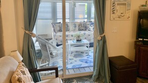 A room with a sliding glass door leading to a balcony, a white wicker chair, a small table with a welcome sign, and a decorative mirror on the wall. - Beach Dreams Coastal Retreat, Pool, Hot Tub, Gym, Pickleball & Minutes to Beach (Wells)
