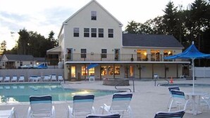 A hotel with a swimming pool, lounge chairs, and a building with multiple windows and a balcony. - Beach Dreams Coastal Retreat, Pool, Hot Tub, Gym, Pickleball & Minutes to Beach (Wells)