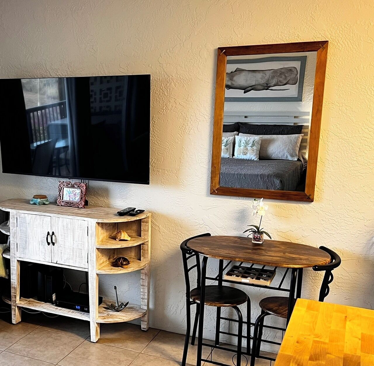 Un soggiorno con televisione a schermo piatto, un mobile in legno, un tavolino rotondo con due sedie e un quadro incorniciato appeso al muro.
