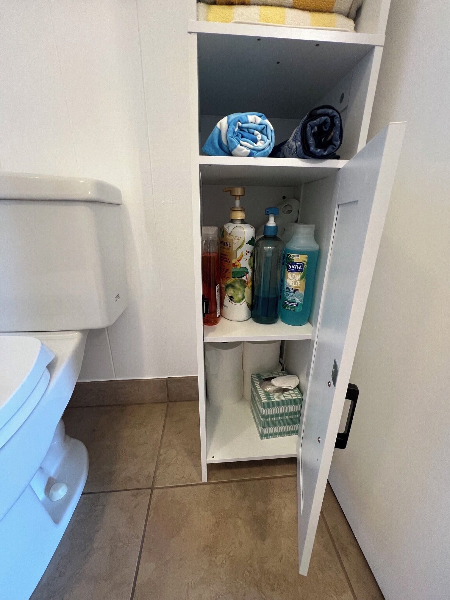 Een badkamer met een toilet, een plank met toiletartikelen en een doos op de vloer.