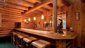 Ein rustikales Blockhaus-Interieur mit einer Holztheke, Hockern, einem großen Spiegel und einer gemütlichen Einrichtung.