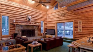 Ein Blockhaus-Interieur mit Kamin, Ledersofas, einem Fernseher und einem Essbereich.