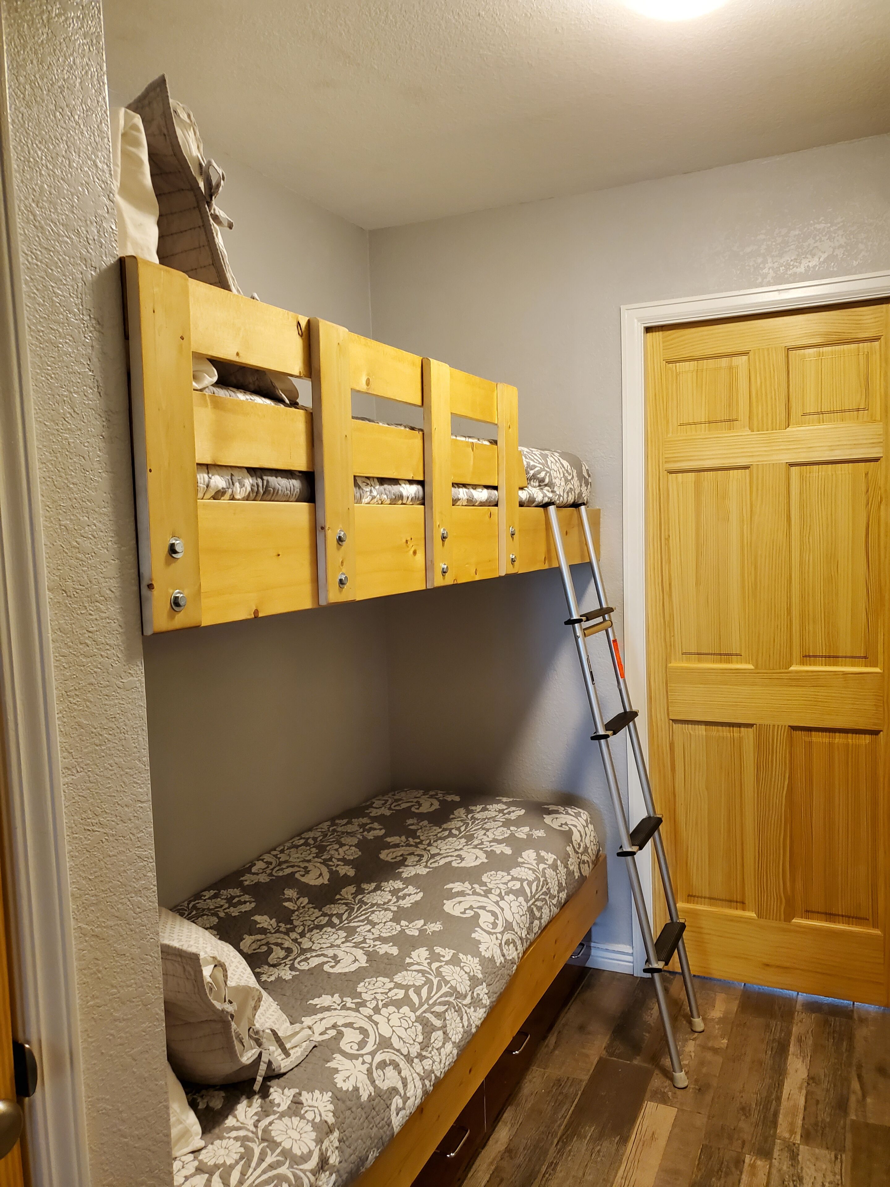 A bunk bed with a ladder, a door, and a patterned bedspread.