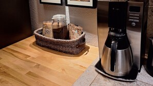 Une cuisine équipée d’une machine à café, d’un panier rempli de bocaux et de tableaux accrochés au mur.